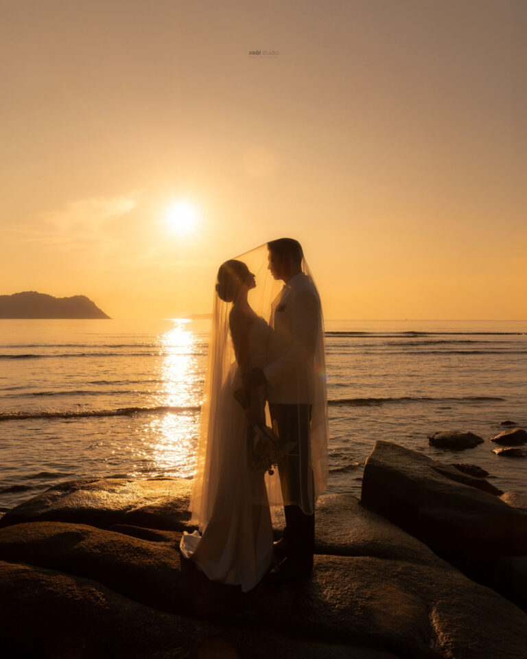 Hà và Thắng đứng đối diện nhau trên bãi đá trước mặt trời buổi sáng.